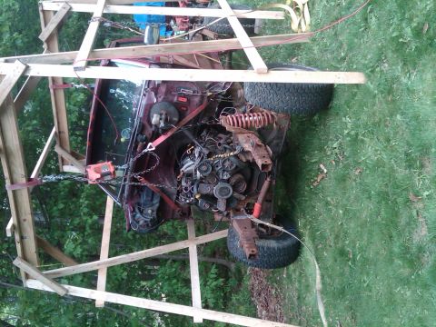 1992 Ford F-150 - The vehicle's engine and chassis are suspended by chains and straps within a wooden frame outdoors.
