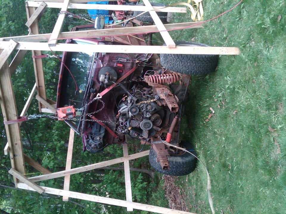 Red 1992 Ford F-150 engine bay with disassembled parts, suspended by wooden frame and chains