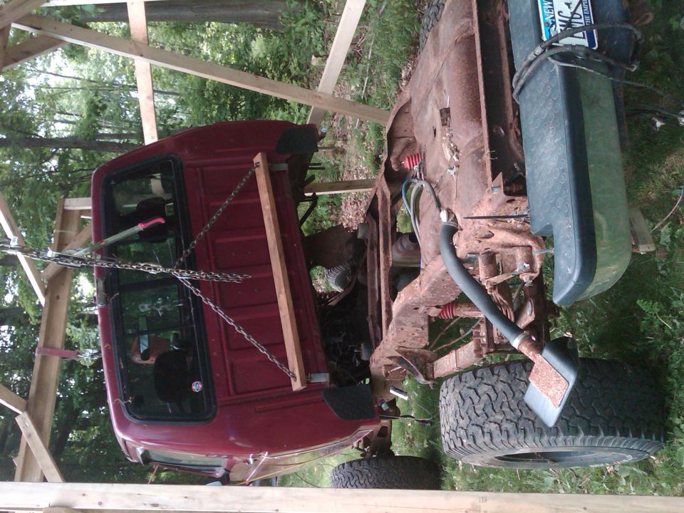 rusted truck chassis with cab, suspended by chains and wood beams