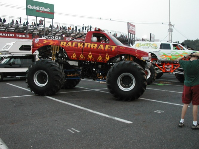 Red monster truck with flames and 'Backdraft' text parked next to a white monster truck