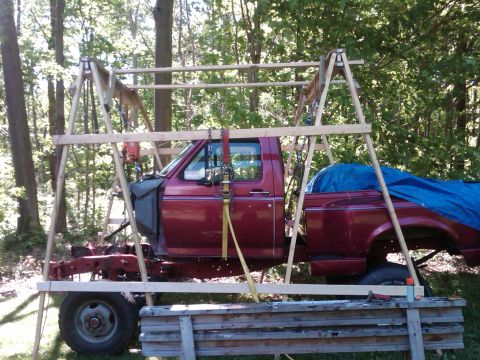 1992 Ford F-150 - A red pickup truck is partially disassembled and supported by a wooden frame outdoors.