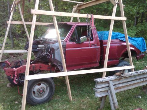 1992 Ford F-150 - A red 1992 Ford F-150 pickup truck is partially disassembled and supported by a wooden frame, suggesting ongoing repairs or modifications.