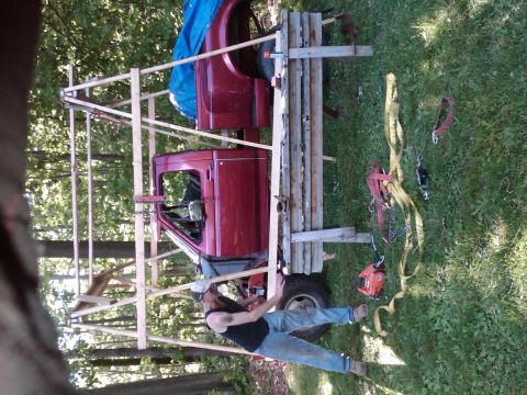 1992 Ford F-150 - A red pickup truck cab and bed section is supported by a wooden frame, with a person working on it outdoors.
