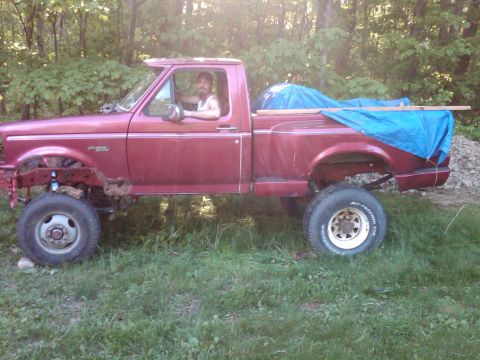 1992 Ford F-150 - A man sits in the driver's seat of a red 1992 Ford F-150 pickup truck parked outdoors.