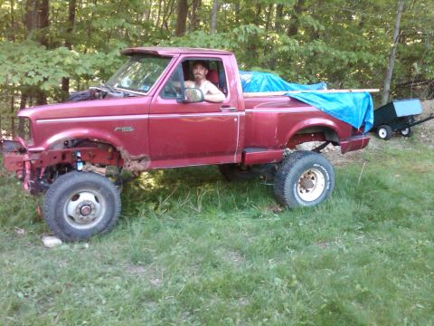 1992 Ford F-150 - A red 1992 Ford F-150 pickup truck is parked in a grassy area with a man in the driver's seat.