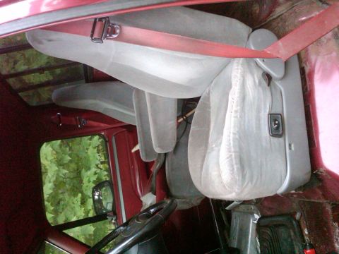 1992 Ford F-150 - The interior of a 1992 Ford F-150 features light gray bench seats and red interior trim, with a view of trees through the window.