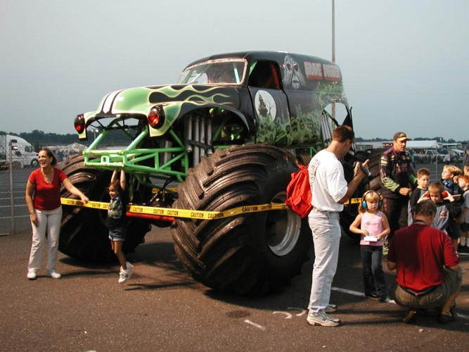 Monster truck with green flames and grim reaper graphics, caution tape in front, people watching