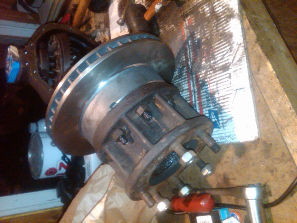Differential housing with gears visible, attached to a brake rotor and hub assembly with lug nuts