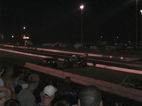 1994 Ford Bronco - Two vehicles, a monster truck and a drag car, compete on a drag strip under stadium lights.