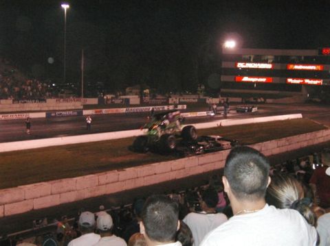 1994 Ford Bronco - A monster truck is seen on top of a car during an event at night, with spectators in the foreground.