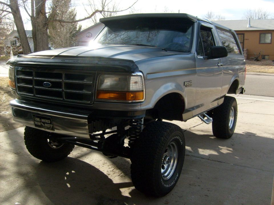 Lifted Ford Bronco parked on a driveway. Has a custom visor and aftermarket wheels