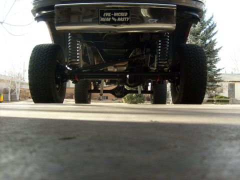 1986 Ford Bronco - The underside of a modified truck is shown, a custom license plate and heavy-duty suspension components.