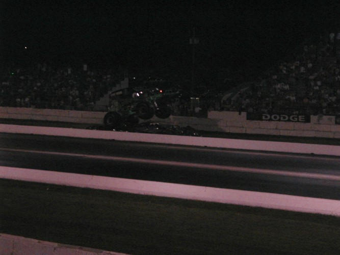 Monster truck airborne over debris at a drag strip at night