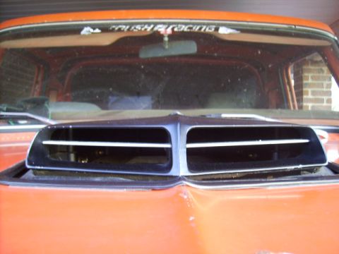 1978 Ford Bronco - Close-up of a dual-nostril hood scoop with black plastic vents mounted on an orange vehicle's hood, viewed from the front. Behind it is a w…