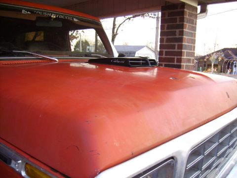 1978 Ford Bronco - Low-angle view across the faded orange hood of a full-size Ford truck, showing a black hood scoop, chrome hood trim and the top of a silver…