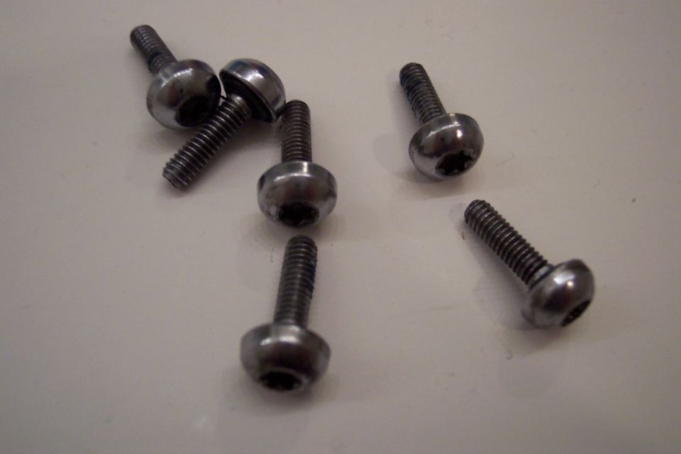 Six metal bolts with hex sockets on a white surface
