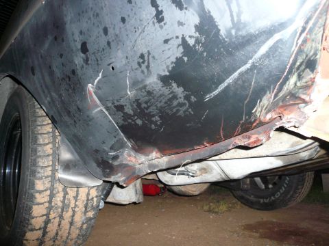1975 Ford Ranchero - The rear quarter panel of a dark-colored vehicle exhibits significant damage, rust, and dents.