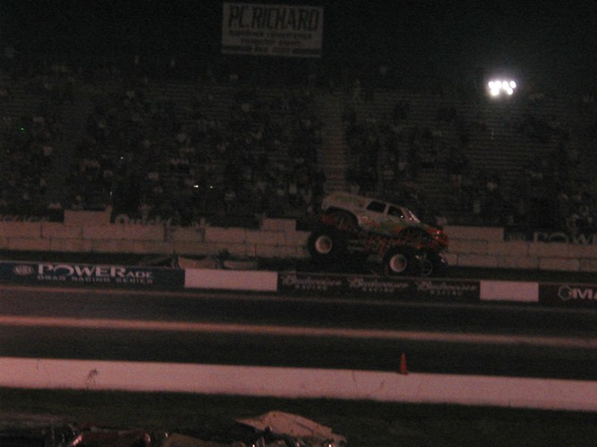 Monster truck with lifted suspension and large tires, viewed from the front-right at a night event