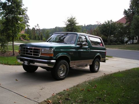 1996 Ford Bronco - This green 1996 Ford Bronco is shown from a three-quarter front view, parked on a paved driveway with a suburban background.