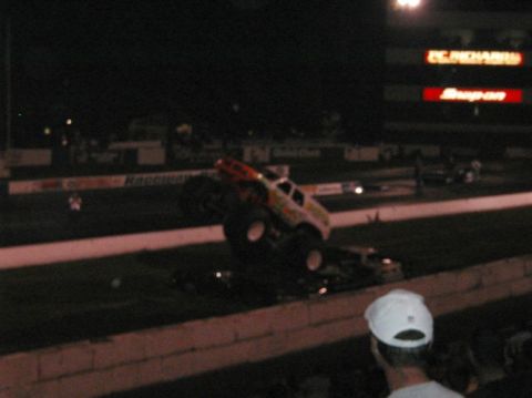1994 Ford Bronco - Monster truck performs a jump over other vehicles during an event at night.