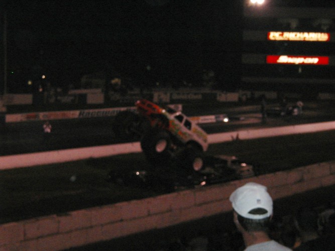 Monster truck mid-air jump over other vehicles at night