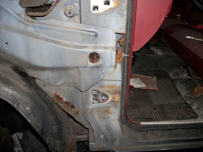 Rusted door jamb and interior floor of a vehicle with red upholstery visible
