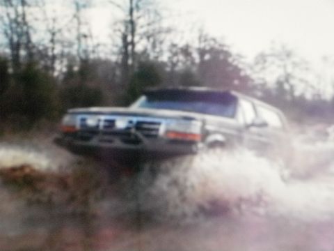 1995 Ford Bronco - This Ford Bronco is navigating through a body of water, kicking up a significant spray.