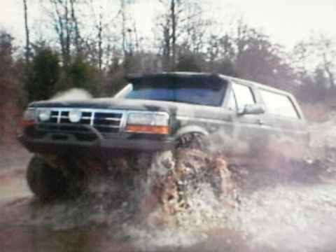 1995 Ford Bronco - A black Ford Bronco navigates through muddy water with its front wheels submerged.