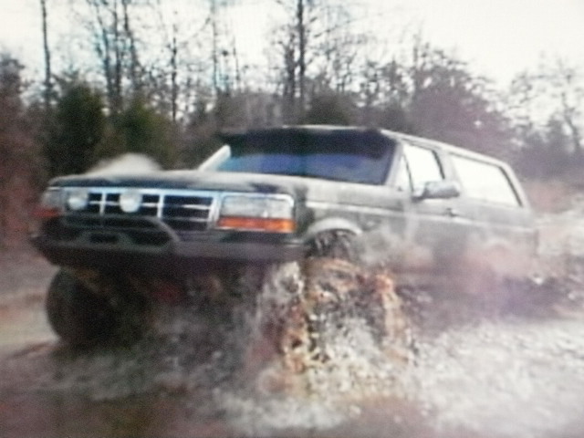 Black Ford Bronco driving through water, front 3/4 view, lifted suspension