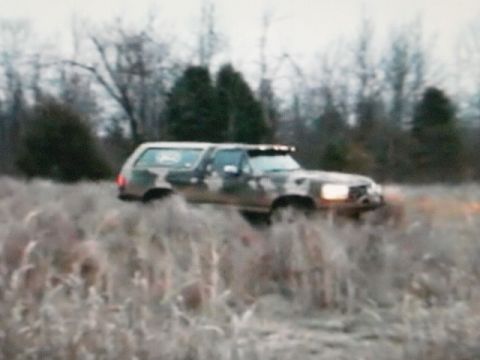 1995 Ford Bronco - Camouflaged Ford Bronco navigates through a field of dry grass and brush.