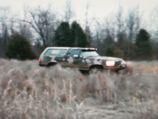 Ford Bronco with camouflage paint driving through tall dry grass