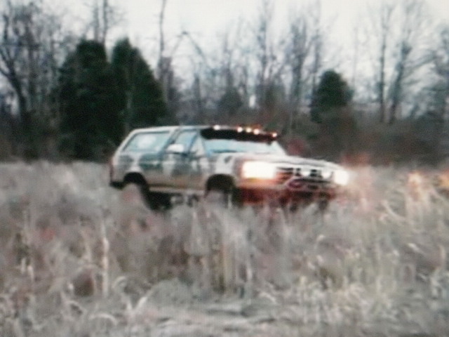 Ford Bronco driving through tall grass with trees in the background