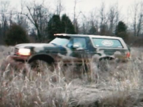 1995 Ford Bronco - A camouflaged Ford Bronco navigates through tall grass in an outdoor scene.