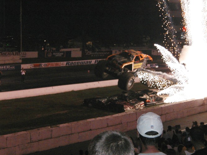 Monster truck mid-air with fireworks, orange and yellow body, large tires