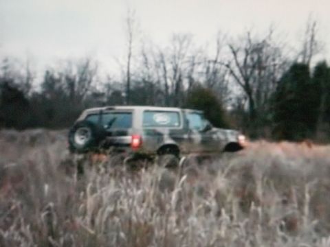 1995 Ford Bronco - 1995 Ford Bronco navigates through a field of tall grass under an overcast sky.