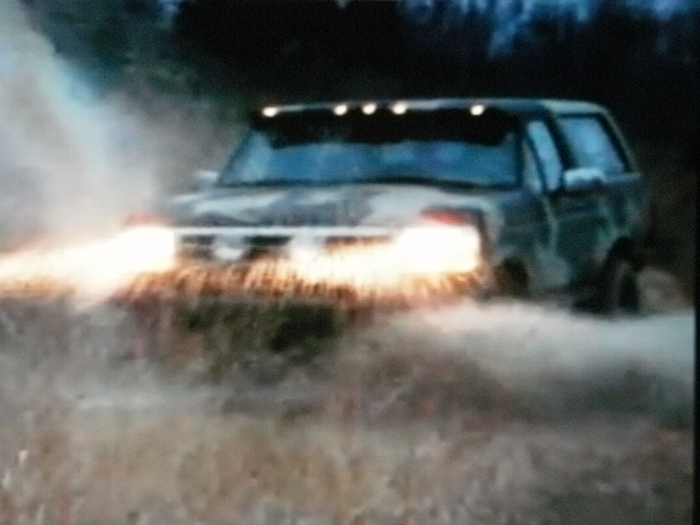 1995 Ford Bronco driving through water with headlights on