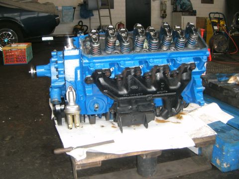 1972 Ford Ranchero - A blue engine with black exhaust manifolds is displayed on a workbench in a garage setting.