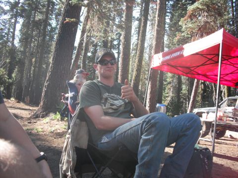 1991 Ford Bronco - A man enjoys a camping trip, giving a thumbs up gesture while seated outdoors near a vehicle.