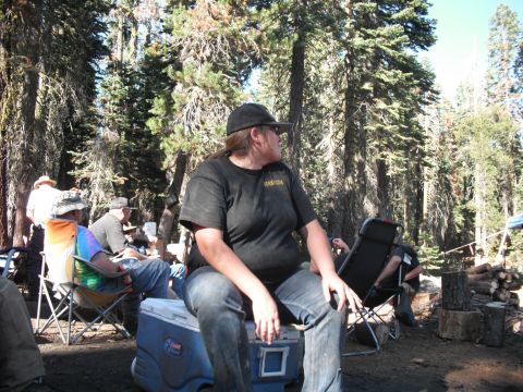 1991 Ford Bronco - Campers relax in a wooded area with trees and logs visible.