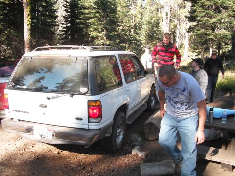 1991 Ford Bronco - A white SUV is parked in a campsite with several people gathered nearby.