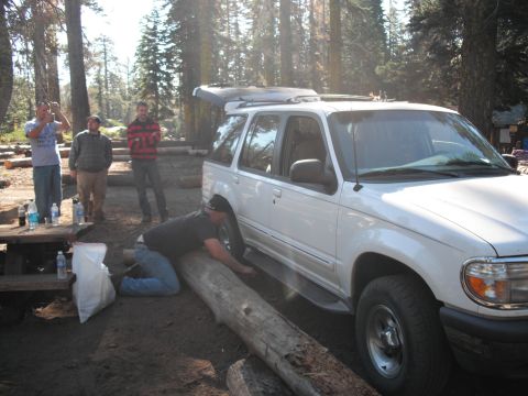 1991 Ford Bronco - People gathered around a white SUV in a wooded area, with one person working on positioning a log.