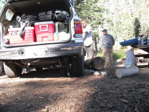 1991 Ford Bronco - SUV packed with camping gear at a campsite with two men and firewood.