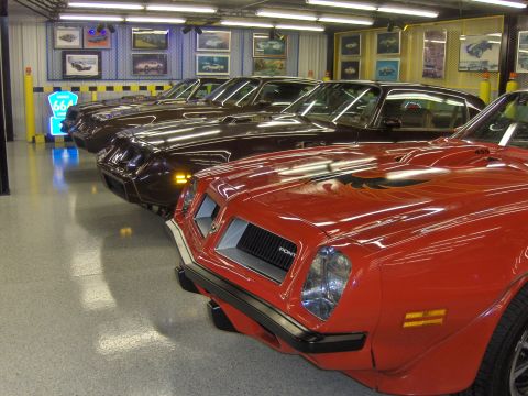 1979 Chevrolet Camaro - Multiple Pontiac Firebirds are parked in a showroom-like garage, with the front of a red one in focus.