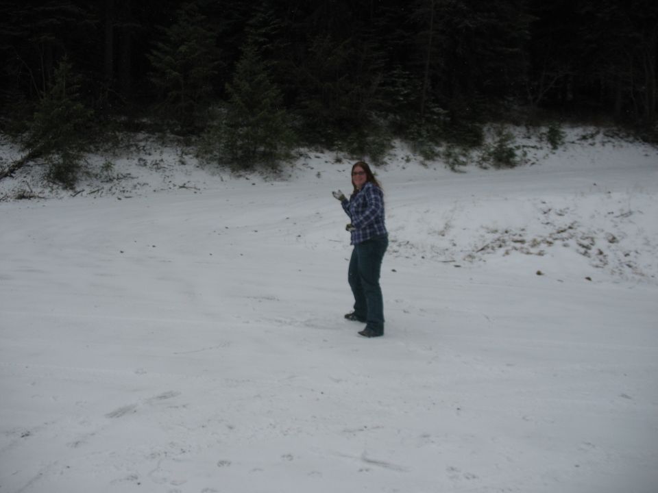 Woman stands in a snow-covered area with trees in the background. Watermark reads SUPERMOTORS