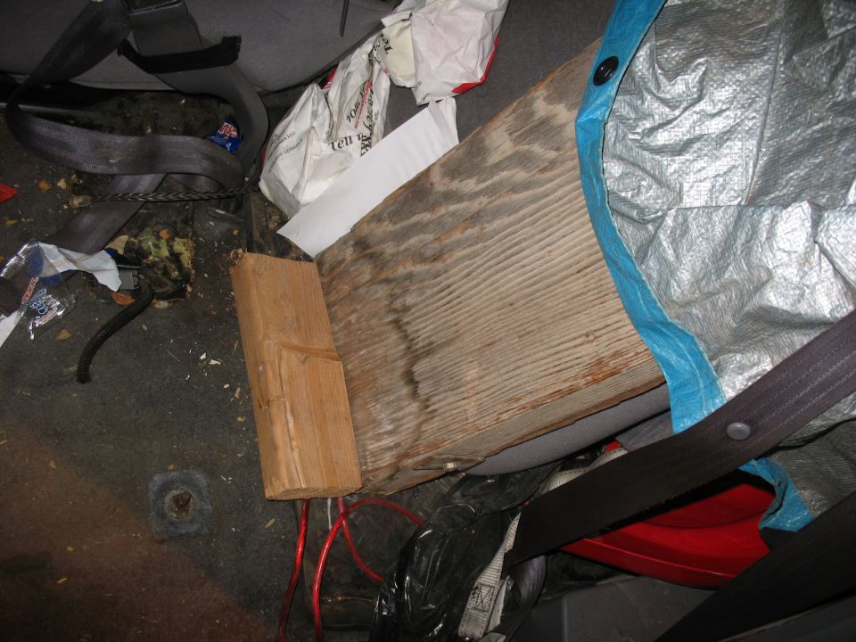 Vehicle interior with debris, a wooden block, and red wires. A tarp is visible