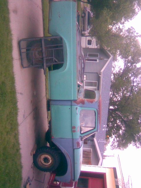 1995 Ford Bronco - A vintage truck cab and chassis sits parked on a driveway next to a house.