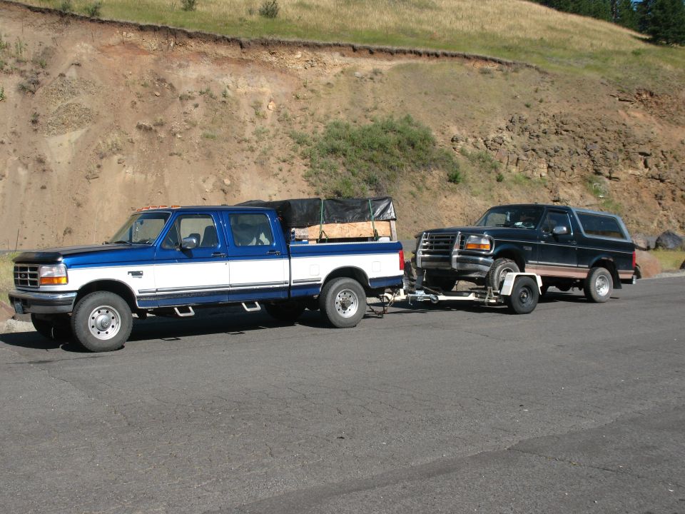 Dark green Ford Bronco on a trailer being towed by a blue and white Ford F-Series pickup truck