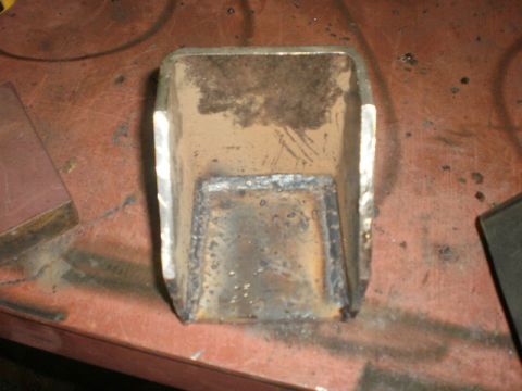 1995 Ford Bronco - A close-up view of a welded metal bracket, likely a vehicle part, resting on a workbench.