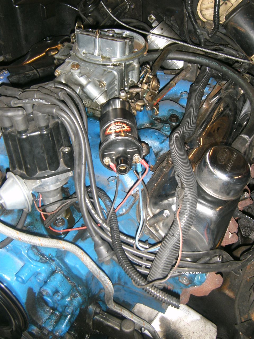 Engine bay with blue block, carburetor, distributor, and ignition coil. Some chrome parts visible
