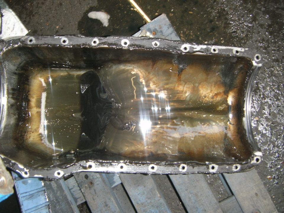 Oil pan with gasket residue and oil residue, resting on wooden beams